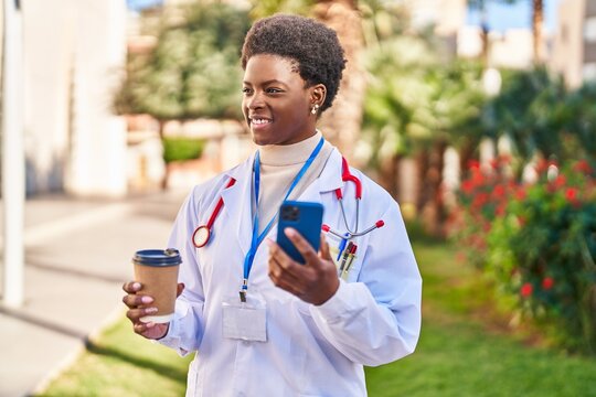 African american woman wearing doctor uniform using smartphone drinking coffee at park
