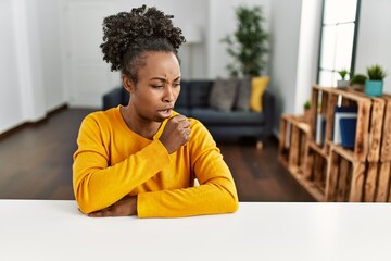 Young african american woman wearing casual clothes sitting on the table at home feeling unwell and coughing as symptom for cold or bronchitis. health care concept.