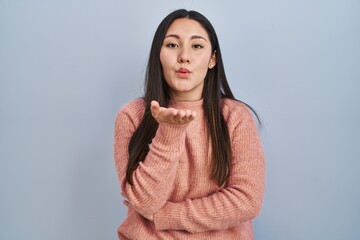 Fototapeta premium Young latin woman standing over blue background looking at the camera blowing a kiss with hand on air being lovely and sexy. love expression.
