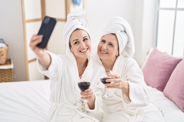 Obraz na płótnie Canvas Mother and daughter make selfie by the smartphone drinking glass of wine at bedroom