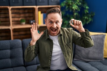 Middle age caucasian man holding virtual currency bitcoin celebrating victory with happy smile and winner expression with raised hands