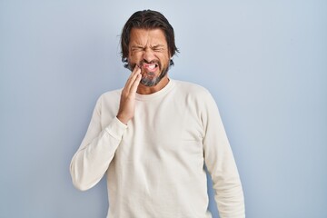 Handsome middle age man wearing casual sweater over blue background touching mouth with hand with painful expression because of toothache or dental illness on teeth. dentist