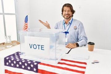 Handsome middle age man sitting at voting stand smiling cheerful presenting and pointing with palm of hand looking at the camera.