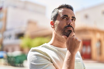 Young hispanic man standing with doubt expression at street