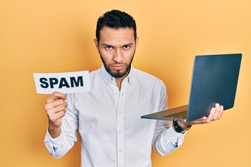 Hispanic man with beard working using computer laptop holding spam banner skeptic and nervous, frowning upset because of problem. negative person.