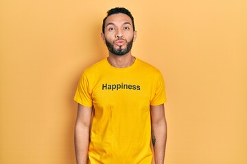 Hispanic man with beard wearing t shirt with happiness word message looking at the camera blowing a kiss on air being lovely and sexy. love expression.
