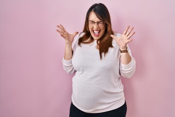 Pregnant woman standing over pink background celebrating mad and crazy for success with arms raised...