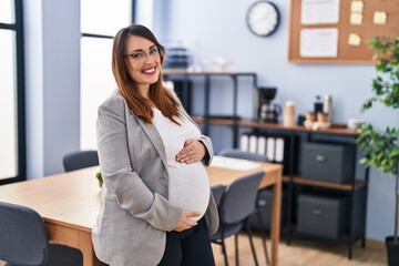 Young pregnant woman business worker smiling confident touching belly at office