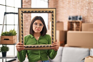 Young hispanic woman at new home holding empty frame depressed and worry for distress, crying angry and afraid. sad expression.