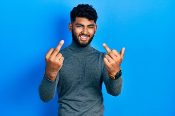 Fototapeta premium Arab man with beard wearing turtleneck sweater showing middle finger doing fuck you bad expression, provocation and rude attitude. screaming excited