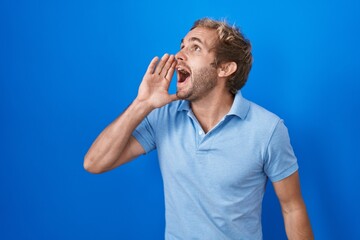 Fototapeta premium Caucasian man standing over blue background shouting and screaming loud to side with hand on mouth. communication concept.