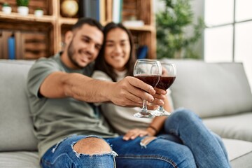 Young latin couple smiling happy toasting with red wine glass at home.