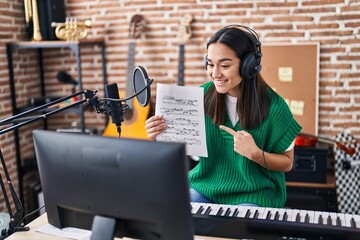 Young south asian woman doing online music tutorial showing music sheet smiling happy pointing with hand and finger