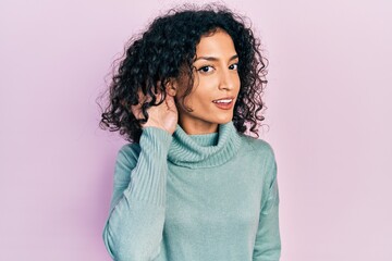 Fototapeta premium Young latin girl wearing casual clothes smiling with hand over ear listening and hearing to rumor or gossip. deafness concept.
