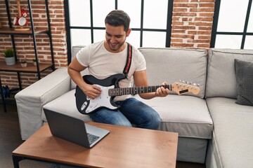 Young hispanic man having online electrical guitar class at home