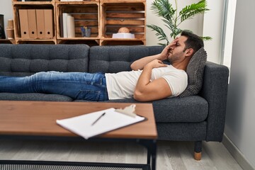 Young hispanic man stressed having mental therapy lying on sofa at psychology center