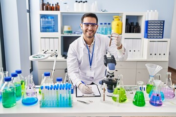 Young hispanic man scientist holding test tube writing report at laboratory