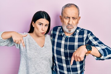 Hispanic father and daughter wearing casual clothes pointing down looking sad and upset, indicating...