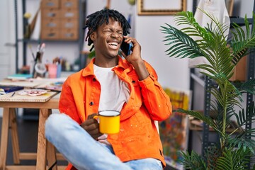 African american man artist drinking coffee talkking on the smartphone at art studio