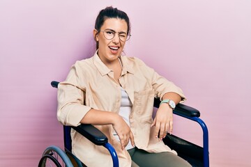Young hispanic woman sitting on wheelchair winking looking at the camera with sexy expression,...