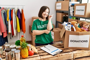 Young down syndrome woman wearing volunteer t shirt at donations stand smiling happy pointing with...