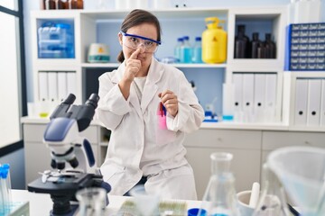 Hispanic girl with down syndrome working at scientist laboratory smelling something stinky and disgusting, intolerable smell, holding breath with fingers on nose. bad smell
