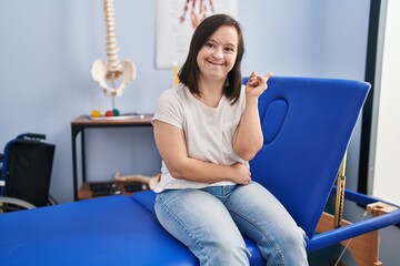 Hispanic girl with down syndrome at physiotherapy clinic smiling happy pointing with hand and...