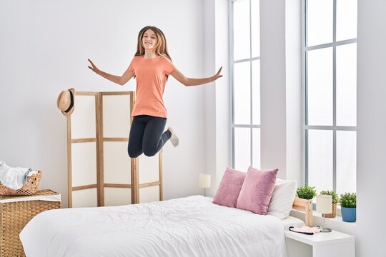Adorable girl smiling confident jumping on bed at bedroom