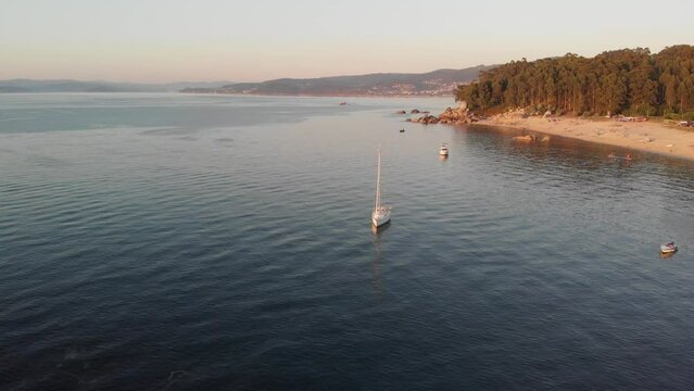 Stunning aerial orbiting camera at Bueu beach, Galicia, Spain.  The warm Spanish sun highlights a beautiful natural shoreline and single yacht