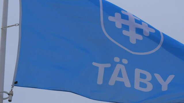 Footage shot in 4K, displaying the logo of T&auml;by municipality (kommun) on a blue flag. Swedish governance and local politics concept.