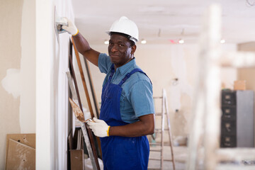 African american contractor doing repairs in a new building plasters the wall indoors