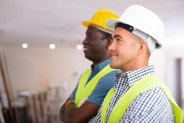 Portrait of positive african-american and caucasian men engineers inspecting construction site.