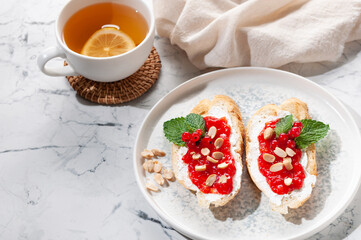 An appetizer of a sandwich with marmalade, red currants and mint greens. Tea with lemon.