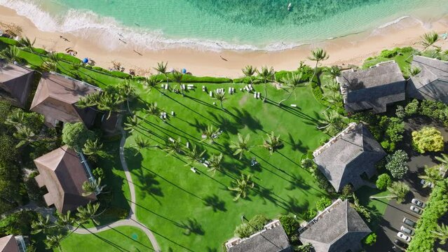Aerial view of resort bungalows at the tiny tropical islet, washed by warm turquoise ocean waters. Cinematic landscape with resort bungalows within juicy green lawn. High quality 4k footage