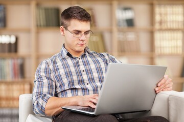 Portrait of smiling man using laptop. Adult male sitting on comfy couch in living room, watching video, taking break