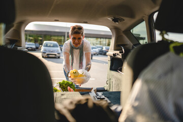 One woman mature caucasian female putting box with vegetables in the back of her car in sunny day...