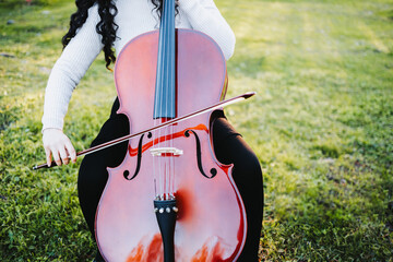close up of a brunette woman with glasses playing cello at sunset in the park, on a green grass.  © padnob