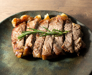 top view of delicious roast beef, on a black plate and wooden surface, with a sprig of thyme on top