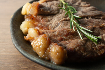 close up shot of delicious roast beef, on a black plate and wooden surface, with a sprig of thyme on top