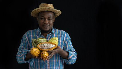 Happy African man or farmer holding cacao or cocoa fruits in arms, looking at camera on black background with copy space.
