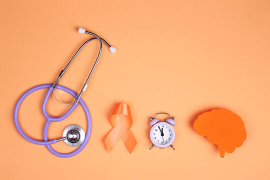World Multiple Sclerosis Day.Orange awareness ribbon, brain symbol, stethoscope and alarm clock on a orange background.