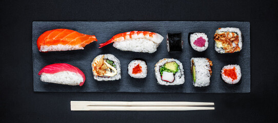 Sushi set on a black slate  background. Japan restaurant menu. Sushi with salmon, tuna and avocado. Top view.