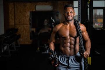 Fototapeta na wymiar Muscular african american man posing with rope in gym. 