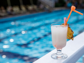 Glass of non alcoholic white coconut Virgin colada cocktail on pool nosing at tropical resort. Horizontal, cocktail on right side. Healthy cold drink. Pool cocktail party. Copy space