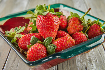Selected fresh strawberries are stacked on green plate on wooden background