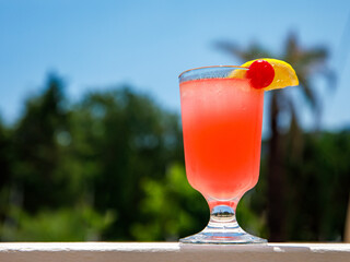 Glass of non alcoholic pink Strawberry lemonade cocktail on table or balcony at tropical resort with palm tree. Horizontal. Healthy fresh cold drink. Vegetarian cocktail party. Copy space