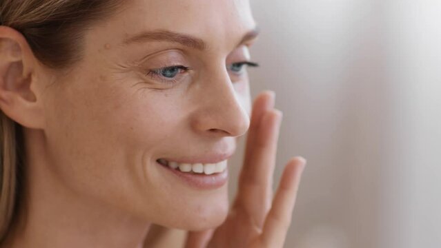 Anti aging skin care. Beautiful middle aged woman with wrinkles applying caring cream on face, empty space