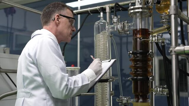 Maintenance service engineer holding paper holder chart check list checking the glass tube syphon information at canabis distillation plant before start up operation 
