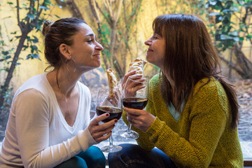 Happy LGBTQ couple eating empanadas and drinking a glass of wine sharing a leisure time at home. Dating, relationship concept.