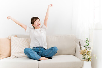 ソファでバンザイしてスッキリ解決した日本人女性（笑顔）
